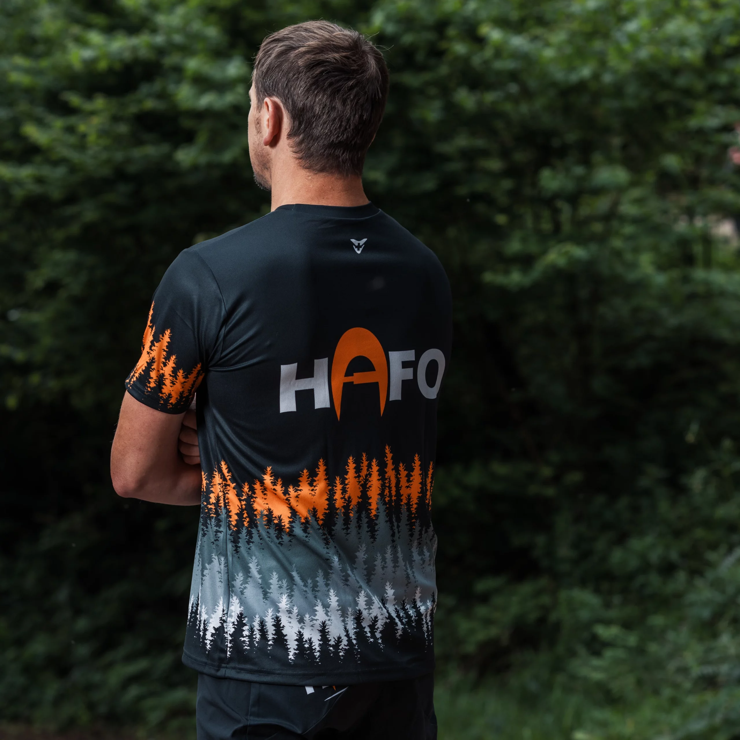 Seitlich von hinten aufgenommener Mann im HAFO-Radshirt mit Rückenaufdruck HAFO und farbigem Baummuster am unteren Rücken und Ärmel.