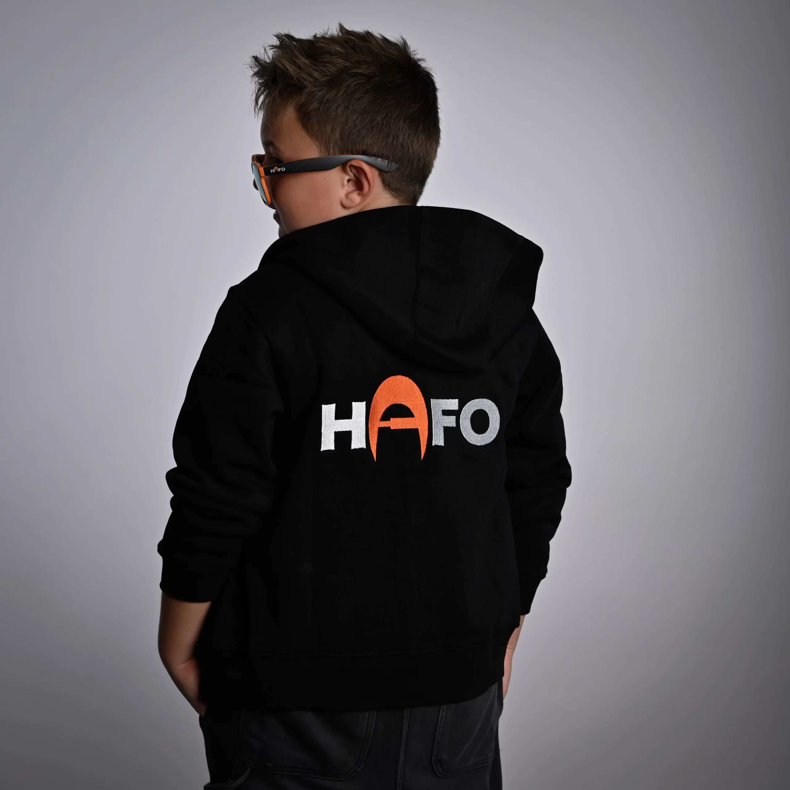 Kind mit dem Rücken zur Kamera im HAFO Hoodie Full Zip Kids. Das Kind schaut zur Seite, auf dem Rücken steht HAFO.