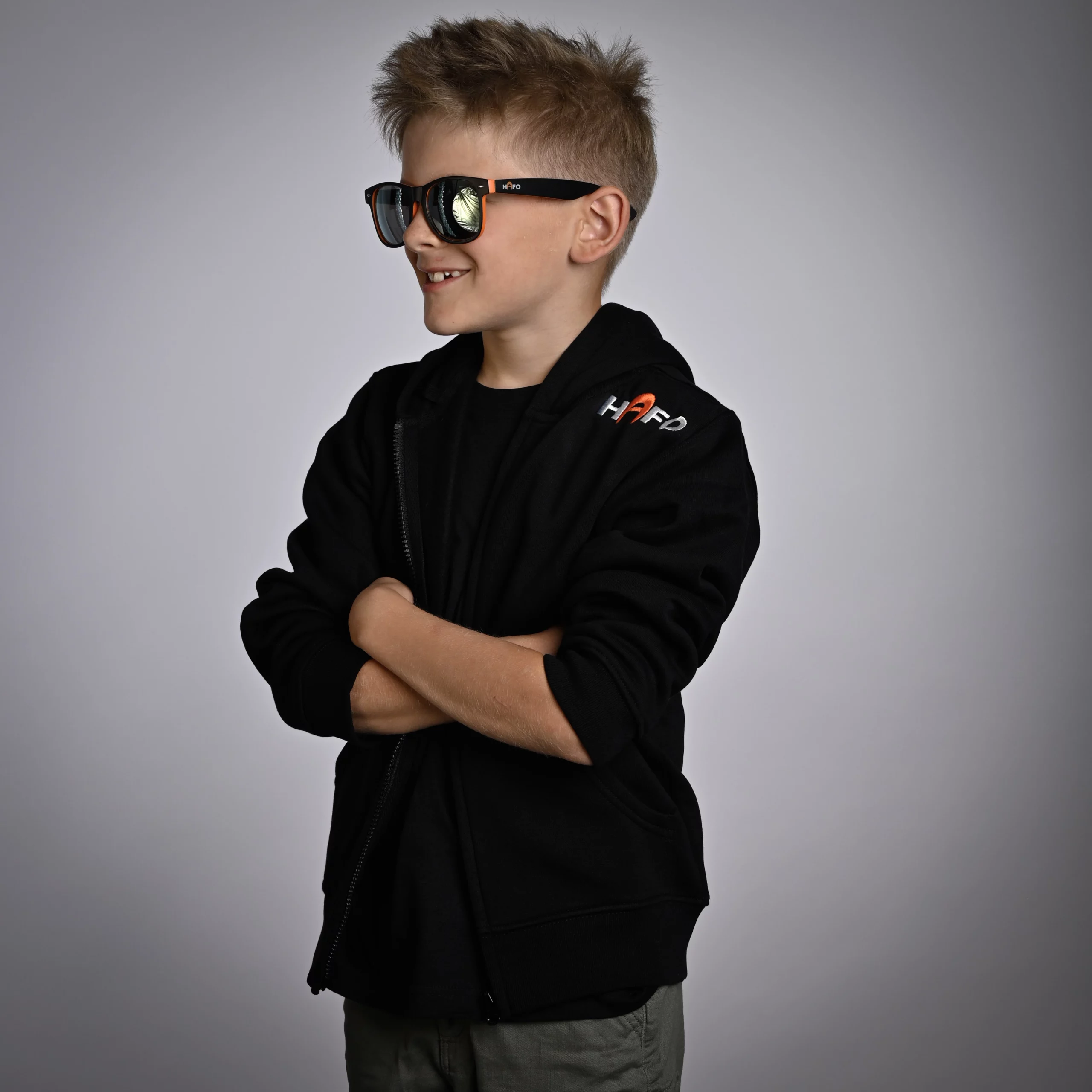 Junge im HAFO Hoodie Full Zip Kids, schräg zur Kamera positioniert. „HAFO“ steht oben rechts auf dem Hoodie, er trägt zusätzlich eine Sonnenbrille von HAFO.