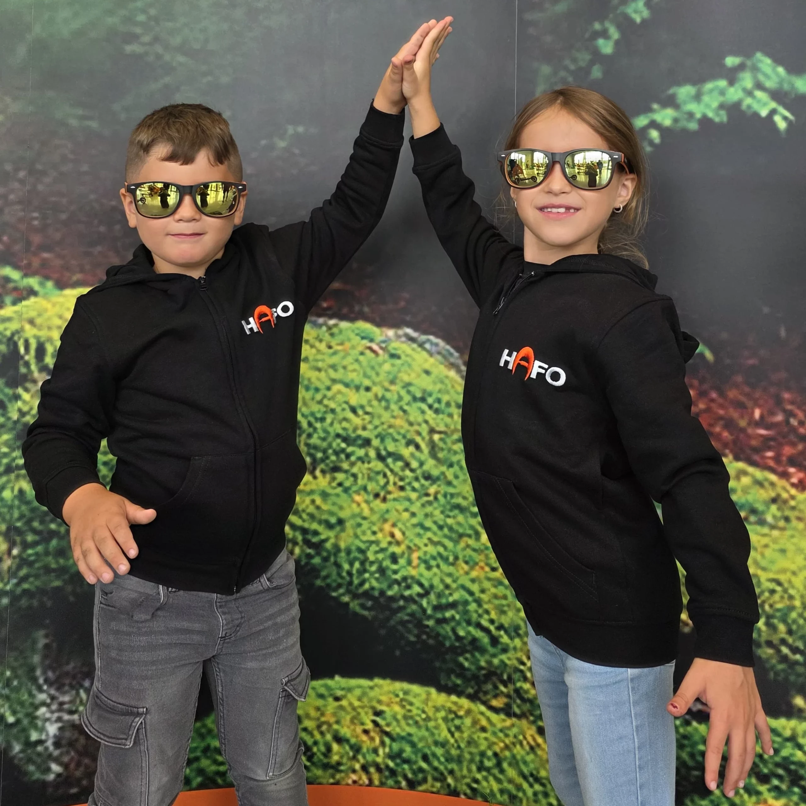 Zwei Kinder klatschen miteinander und tragen HAFO Full Kids Hoodies sowie HAFO-Sonnenbrillen.