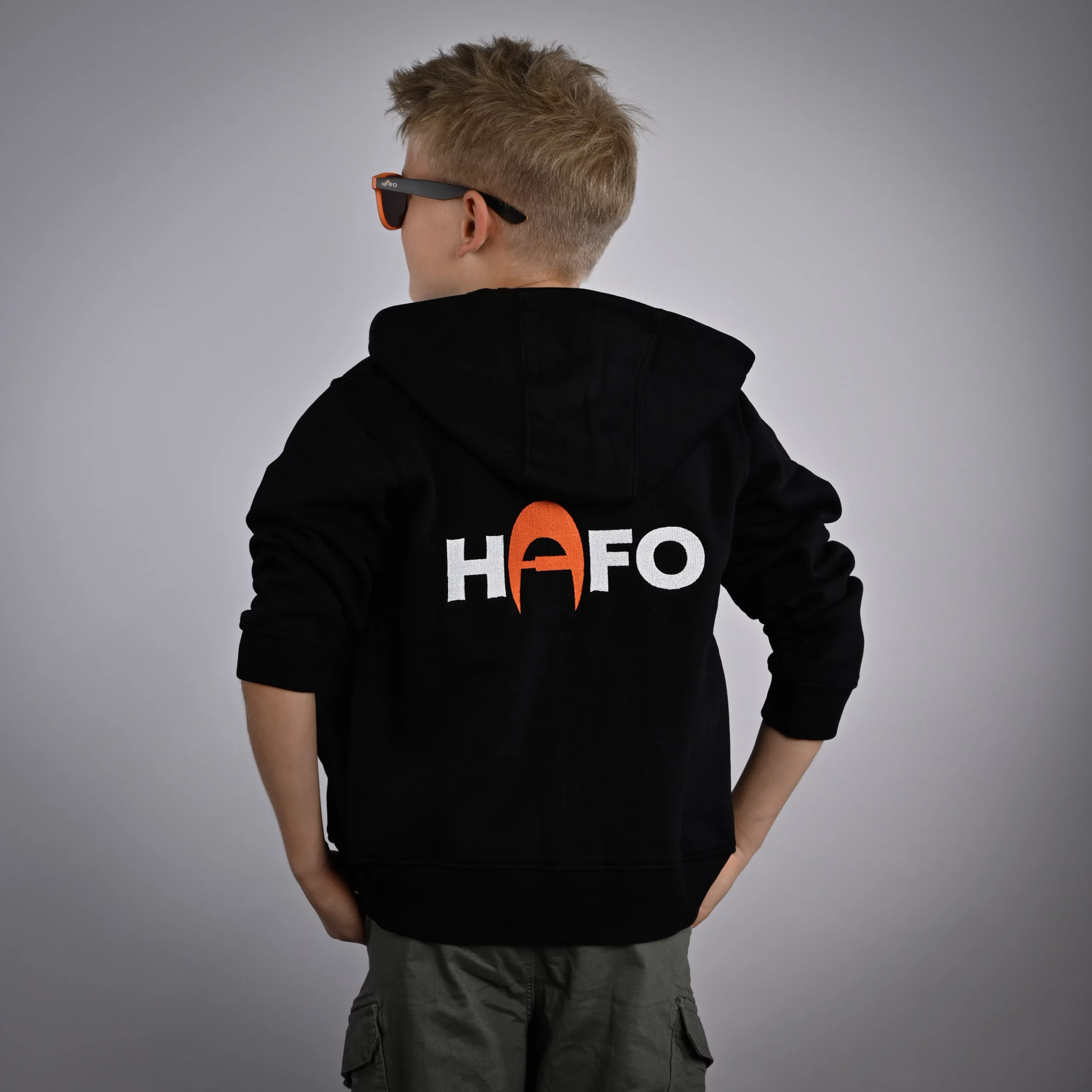 Ein Kind steht mit dem Rücken zur Kamera und trägt den HAFO Hoodie Full Zip Kids. Der Kopf ist seitlich gedreht, auf dem Rücken des Hoodies steht HAFO.
