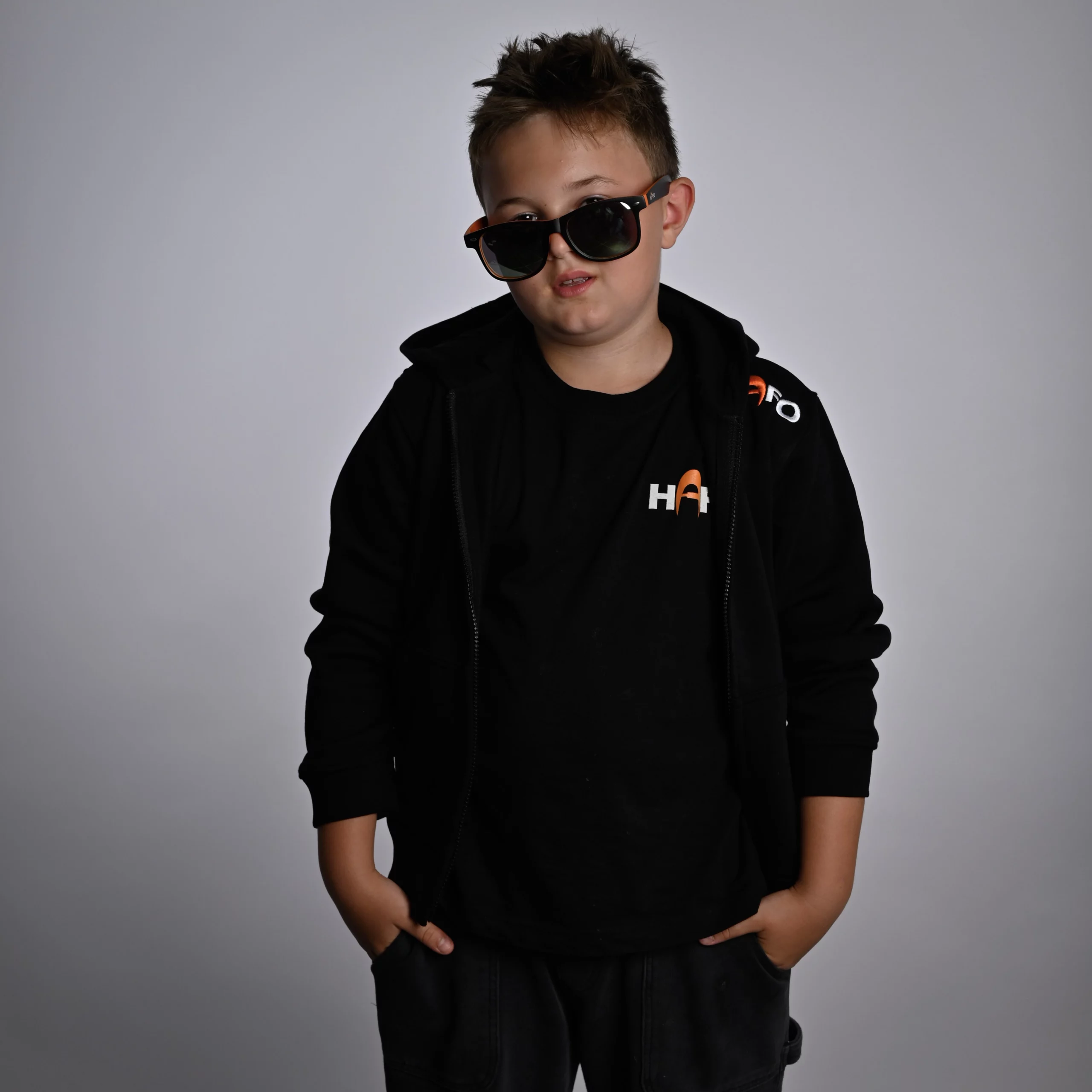 Ein Junge steht frontal zur Kamera und trägt den HAFO Hoodie Full Zip Kids. Er trägt zusätzlich eine Sonnenbrille von HAFO.